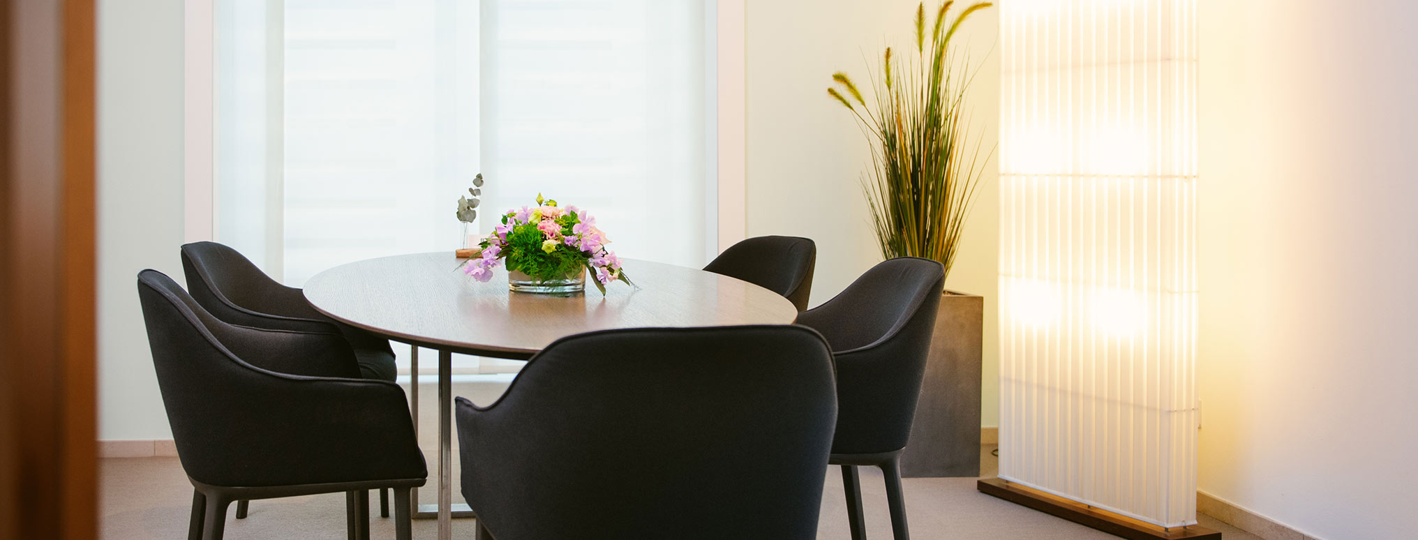 Stilvoll eingerichteter Beratungsraum mit rundem Tisch, schwarzen Stühlen und dezentem Blumenschmuck.